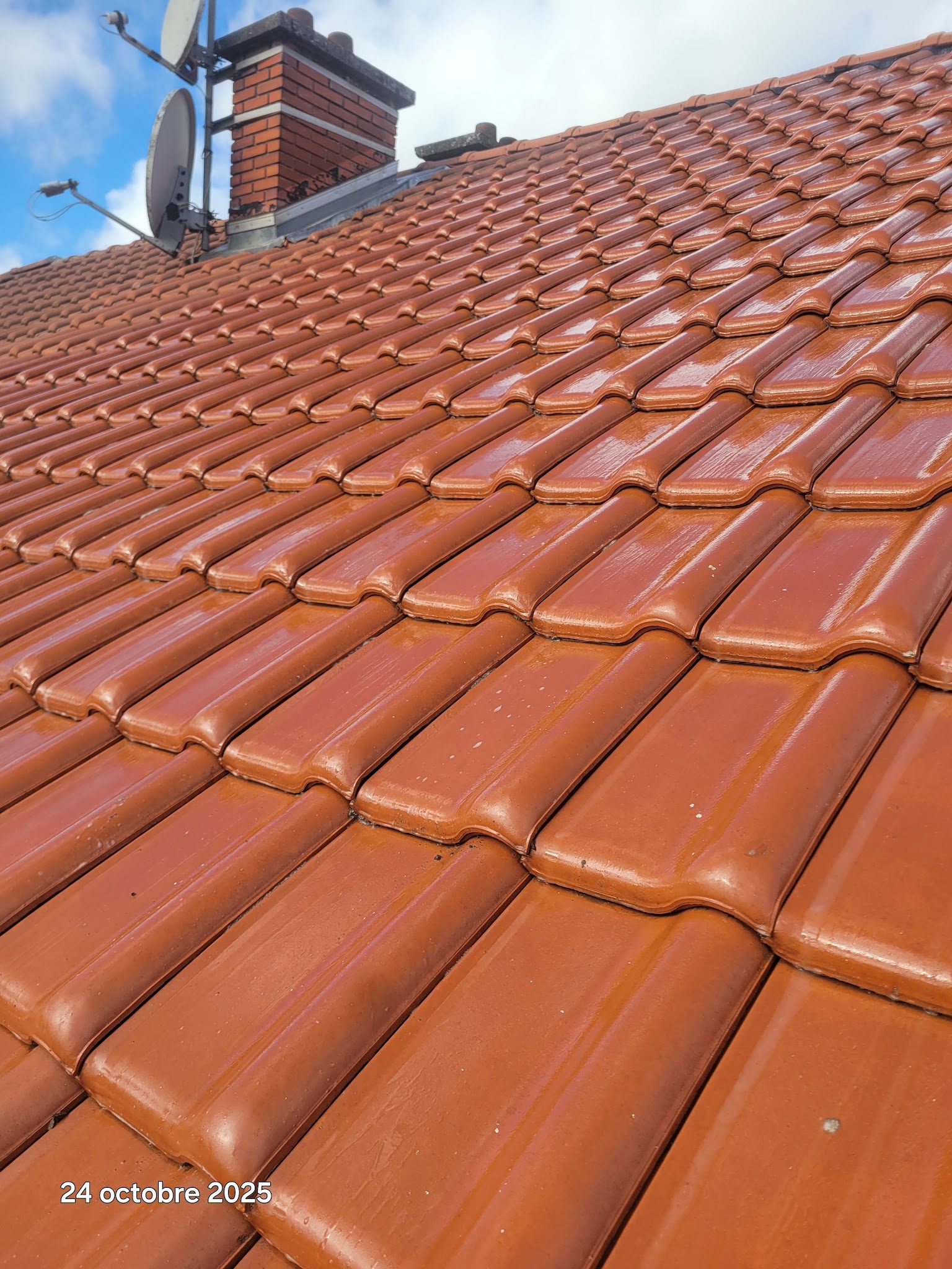Toiture en tuiles rouges brillantes après traitement, avec la cheminée en brique